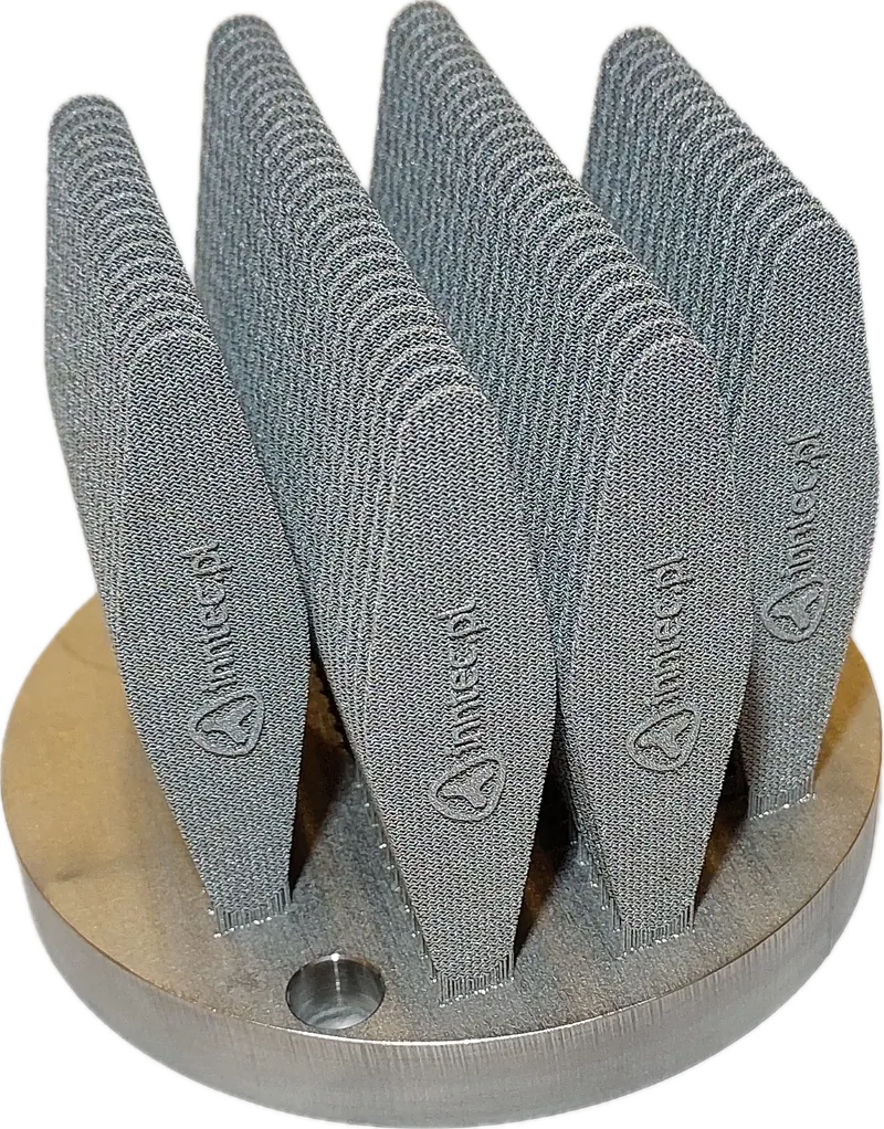 Metalowe wydruki 3D z logo inntec.pl na płycie roboczej, wykonane w technologii LPBF